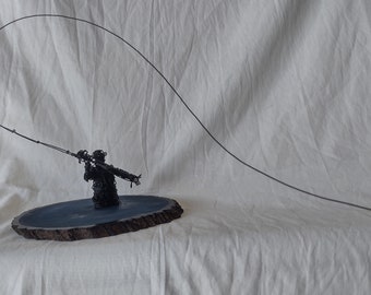Escultura de pescador de alambre de acero sobre rodaja de pino