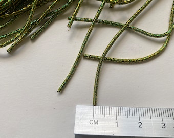 May include: A pile of green and gold elastic cord with a ruler measuring 3 centimeters. The cord is approximately 1/8 inch thick.