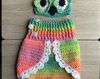 May include: A rainbow striped crochet baby outfit with a matching owl hat. The hat has white and black eyes and a black beak. The outfit has a white crocheted lace trim.