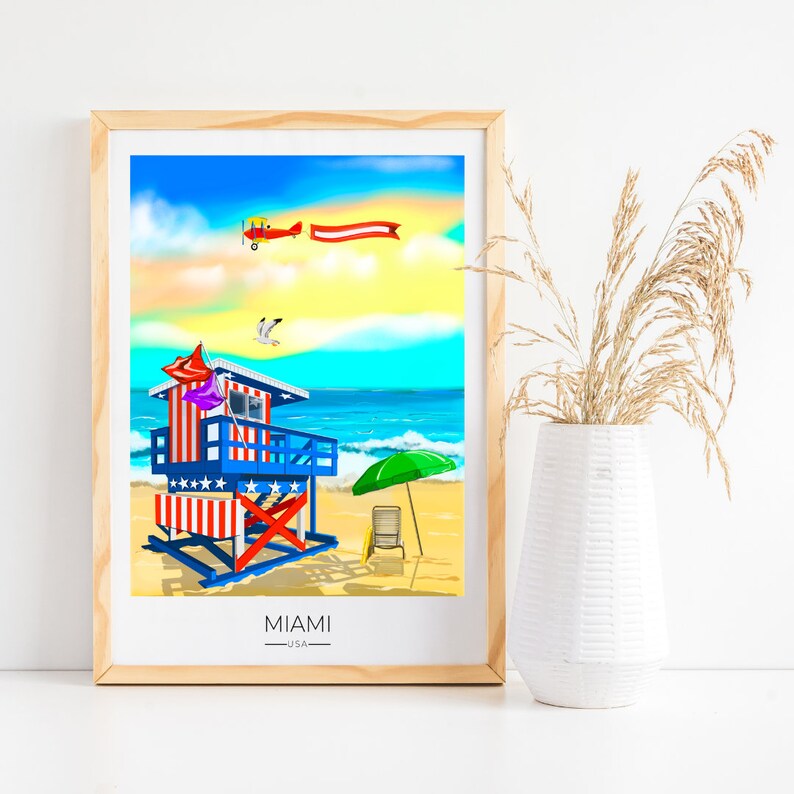 May include: A framed art print featuring a vibrant beach scene. A lifeguard stand with red, white, and blue stripes and accents stands on a sandy beach. A red biplane flies in the sky, and the word "MIAMI" is printed at the bottom.