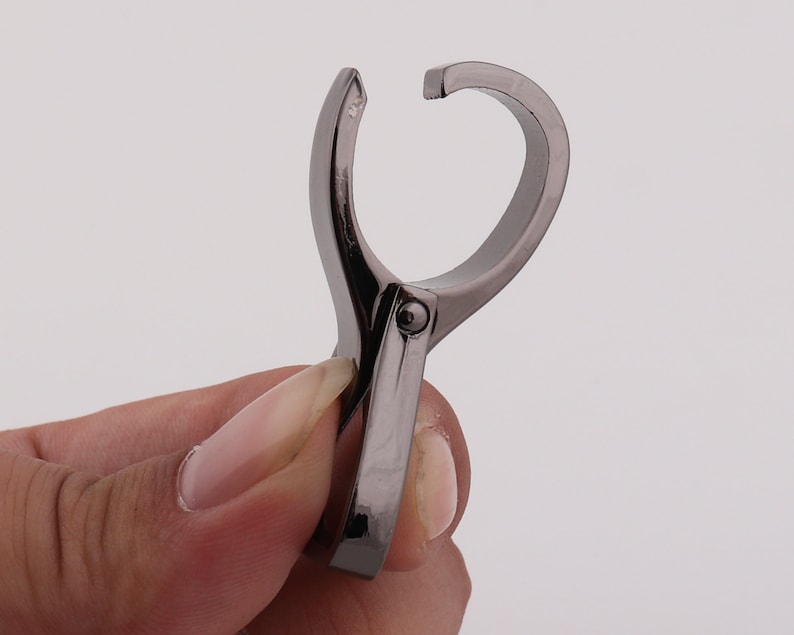 May include: A silver-toned metal clip with a rounded opening. The clip is designed to hold items together.