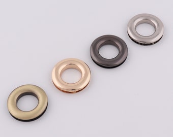 May include: Four metal grommets in different finishes: gold, silver, black, and bronze. The grommets are round with a raised edge and a hole in the center.