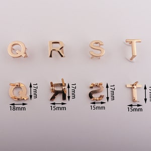 May include: Gold-colored metal letter charms in the shape of the letters Q, R, S, and T. The charms are approximately 1.5 inches tall and 1 inch wide. The charms are shown on a white background.