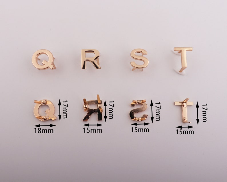 May include: Gold-colored metal letter charms in the shape of the letters Q, R, S, and T. The charms are approximately 1.5 inches tall and 1 inch wide. The charms are shown on a white background.