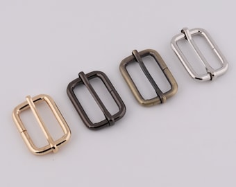 May include: Four metal slider buckles in different finishes: gold, silver, black, and antique brass. The buckles are rectangular with a center bar and are commonly used for straps, belts, and bags.