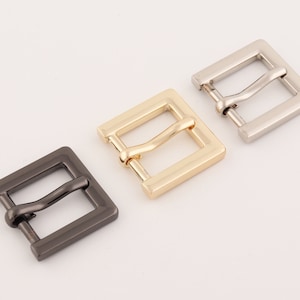 Può includere: Tre fibbie per cintura in metallo in diverse finiture: argento, oro e nero. Ogni fibbia è di forma quadrata con una superficie liscia e lucida.