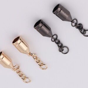 May include: Two sets of gold and black metal end caps with attached chains. The end caps are cylindrical with a pointed end. The chains are made of small, linked metal rings.
