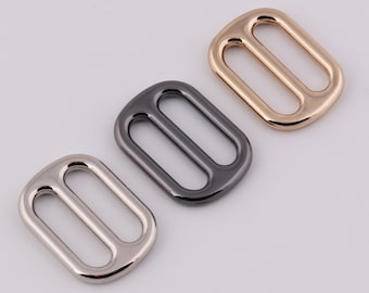 May include: Three metal slider buckles in different finishes: silver, black, and gold. Each buckle has a rectangular shape with two oval-shaped holes.