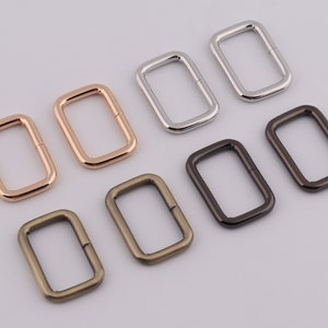 Op de afbeelding: Acht rechthoekige metalen ringen in verschillende maten en afwerkingen. De ringen zijn zilver, goud en brons.