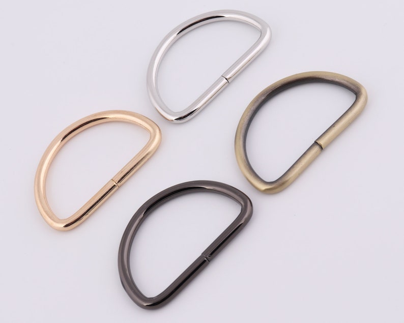 May include: Four D-shaped metal rings in different finishes: silver, gold, antique brass, and black.