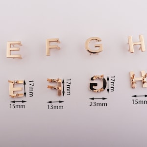 May include: Gold-toned metal letter charms in the shape of the letters E, F, G, and H. The charms are approximately 1.7 cm tall and range in width from 1.3 cm to 2.3 cm.