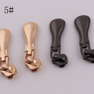 May include: Four zipper pulls, two gold and two black. The gold pulls have a decorative design and the black pulls have a smooth finish.