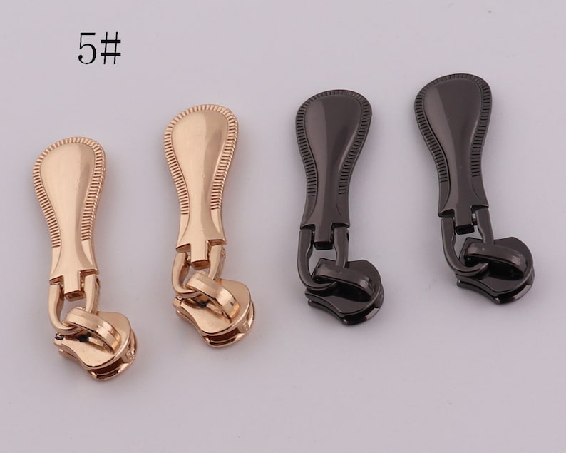 May include: Four zipper pulls, two gold and two black. The gold pulls have a decorative design and the black pulls have a smooth finish.