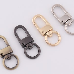 May include: Four metal keychains with different finishes: antique brass, black, gold, and silver. Each keychain has a swivel hook and a D-ring.