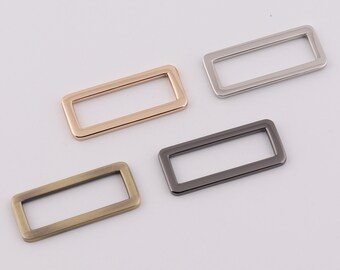 Puede incluir: Cuatro anillos rectangulares de metal en diferentes acabados: oro, plata, negro y latón antiguo.
