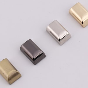 May include: Four metal rectangular-shaped bag hardware pieces in different finishes: gold, silver, black, and antique gold.