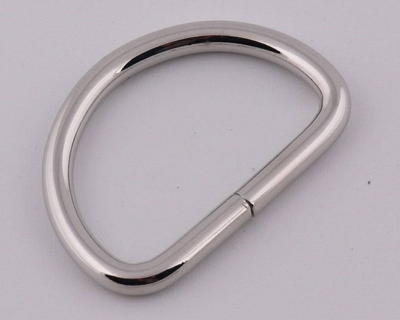 Pu&ograve; includere: Un anello a D in metallo argentato con una finitura liscia e lucida. L'anello &egrave; aperto da un lato e chiuso dall'altro.