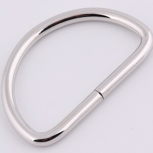 May include: A silver metal D-ring with a smooth finish. The ring is open on one side and has a closed loop on the other.