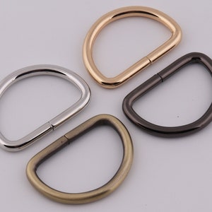 Pu&ograve; includere: Quattro anelli a D in metallo in diverse finiture: oro, argento, ottone anticato e nero. Gli anelli sono tutti della stessa dimensione e forma, e sono perfetti per essere fissati a borse, cinture o altri accessori.