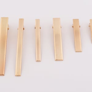 Puede incluir: Conjunto de seis pinzas para el pelo de metal dorado en varios tamaños. Las pinzas son rectangulares y tienen un acabado liso y pulido.