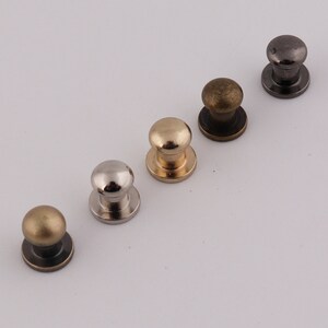 May include: Five metal dome-shaped knobs in different finishes: silver, gold, brass, and black. The knobs have a round base and are used for furniture or crafts.