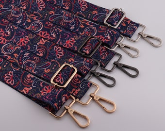 Può includere: Cinque chiusure metalliche di diversi colori per una tracolla per borsa. La tracolla è in tessuto blu scuro con un motivo paisley rosso, bianco e oro.