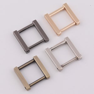 May include: Four metal square-shaped rings in different finishes: gold, silver, black, and antique brass. The rings are about 1 inch in size and have a flat, rectangular shape.