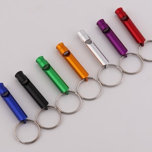 May include: Seven different colored keychains with whistles attached. The keychains are silver, purple, red, orange, green, black, and blue.