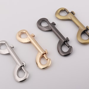 May include: Four metal double-ended snap hooks in silver, gold, gunmetal, and antique brass finishes. These swivel snap hooks are designed for attaching to a variety of items, such as pet leashes, bags, or keychains. The hooks are shown on a white background.