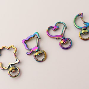May include: Four iridescent metal keyrings with different shapes: a leaf, a cat, a heart, and a crescent moon. Each keyring has a swivel clasp.