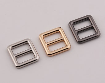 May include: Three metal square-shaped buckles with a rectangular opening in the center. The buckles are silver, gold, and black.