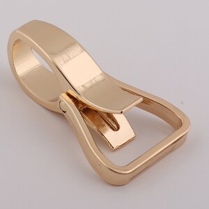 May include: Gold-toned metal swivel hook with a rectangular loop. The hook is designed to attach to a belt or strap.