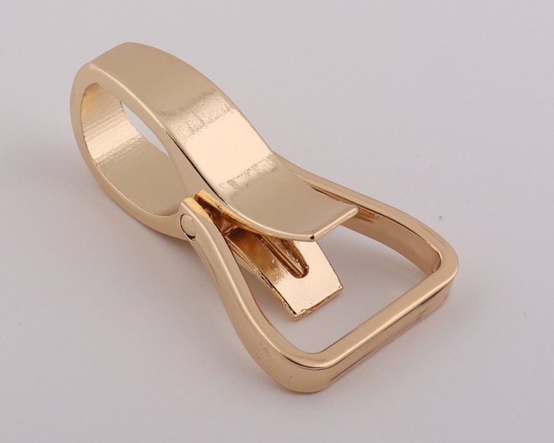 May include: Gold-toned metal swivel hook with a rectangular loop. The hook is designed to attach to a belt or strap.