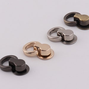 Op de afbeelding: Vier metalen sluitingen in verschillende afwerkingen: goud, zilver, zwart en brons. Elke sluiting heeft een ronde ring en een platte, ronde basis.