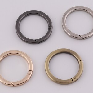 Könnte beinhalten: Vier Schlüsselringe aus Metall in verschiedenen Ausführungen: Silber, Schwarz, Gold und Roségold. Jeder Ring hat einen federbelasteten Verschluss.