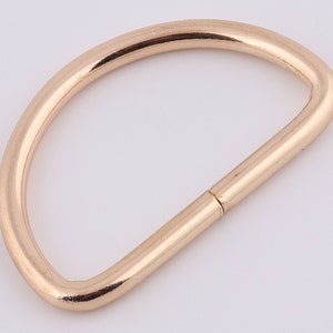 May include: A gold-colored metal D-ring, a type of hardware used for attaching straps, chains, or other accessories.