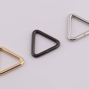 Könnte beinhalten: Drei dreieckige Metallringe in Gold, Silber und Schwarz.