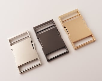May include: Three metal belt buckles in different finishes: silver, black, and gold. The buckles are all the same size and shape, with a rectangular design.