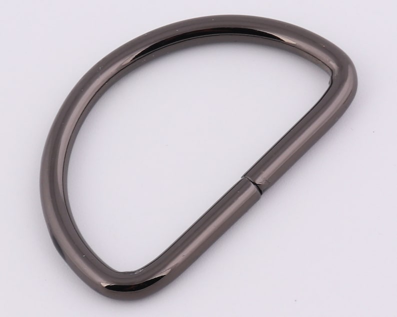 May include: A black metal D-ring with a smooth finish. The ring is open on one side and has a closed loop on the other.