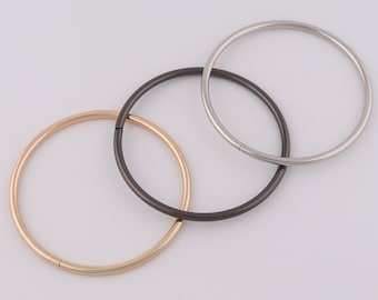 Op de afbeelding: Drie metalen ringen in verschillende maten en kleuren: goud, zilver en zwart. De ringen zijn allemaal rond en hebben een gladde afwerking.