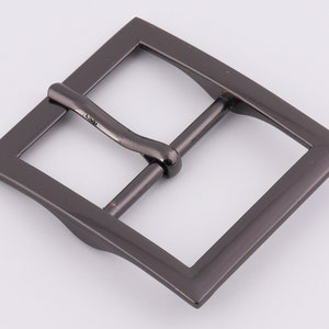 May include: A black metal belt buckle with a rectangular shape and a smooth, slightly curved surface.