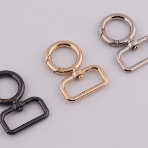 Könnte beinhalten: Drei Metall-Drehverschlüsse mit einer rechteckigen Schlaufe. Die Verschlüsse sind in Silber, Gold und Schwarz.