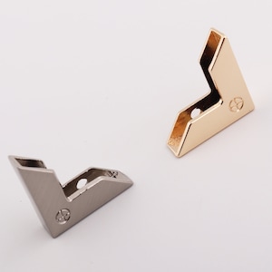 Può includere: Due protezioni per angoli in metallo, uno dorato e uno argentato. Entrambi hanno un piccolo design circolare al centro.