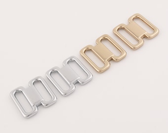 May include: Three metal bra strap adjusters in silver and gold. The adjusters are made of metal and have a rectangular shape with two holes on each side.