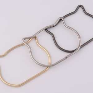 Puede incluir: Tres llaveros de metal con forma de gato en dorado, plateado y gris oscuro.