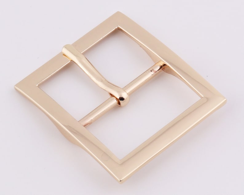 May include: A gold-toned metal belt buckle with a square frame and a smooth, polished finish.