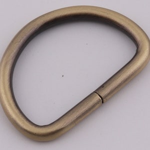 Pu&ograve; includere: Un anello a D in metallo dorato con una finitura liscia. L'anello &egrave; aperto da un lato e chiuso dall'altro.