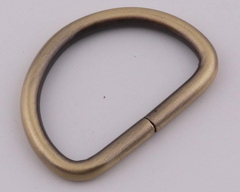 Pu&ograve; includere: Un anello a D in metallo dorato con una finitura liscia. L'anello &egrave; aperto da un lato e chiuso dall'altro.