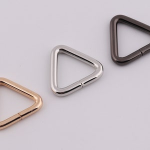 May include: Three triangle-shaped metal rings in gold, silver, and black.