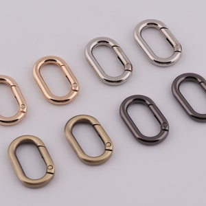 Könnte beinhalten: Sortiment von acht Schlüsselringen aus Metall in verschiedenen Ausführungen, darunter Silber, Gold und Schwarz. Die Schlüsselringe sind oval geformt mit einer glatten Oberfläche.
